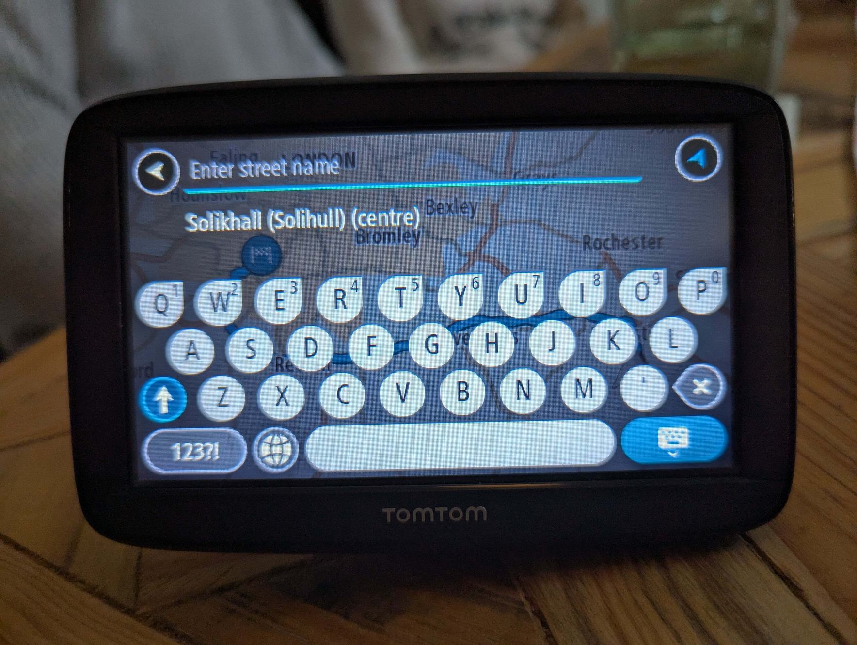 A touch screen TomTom device with various input elements including a key pad and a search field with placeholder text: Enter street name. The placeholder text is pale blue overlaid on a map making it difficult to read.