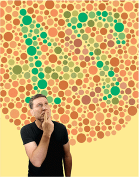 Simon (a clean shaven middle-aged white male with brown hair) standing with one finger place on his mouth and a curious look on his face. Behind him on a yellow background is an Ishitani colour blindness test card (lots of coloured circles at different sizes)
